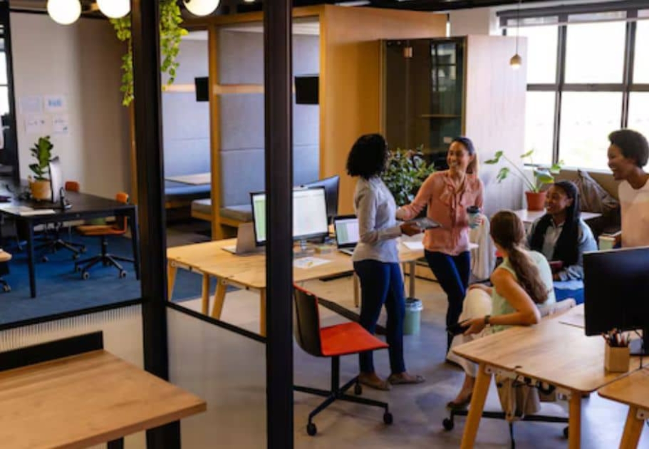 A group of diverse professionals engaging in networking and discussions in a modern coworking space in Hyderabad, featuring open desks, laptops, and a collaborative work environment.